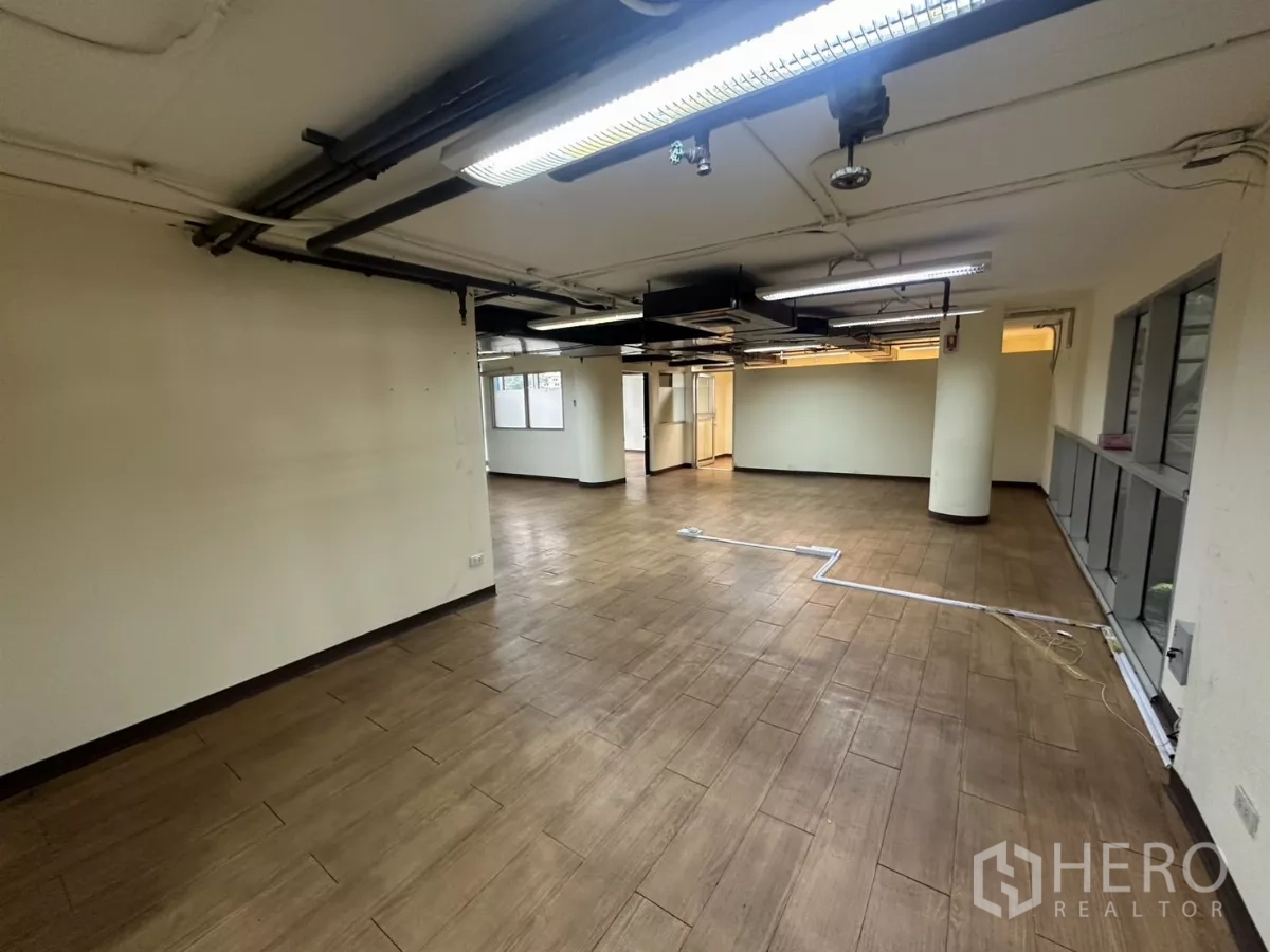 货栈 出租 - 开放式空调仓库办公区，木纹地砖、外露管道、立柱与日光灯。