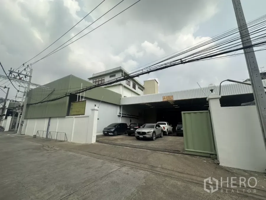 Warehouse for rent in Yan Nawa, Bangkok - Street view of a gated warehouse complex in Yan Nawa with green metal cladding and front parking.