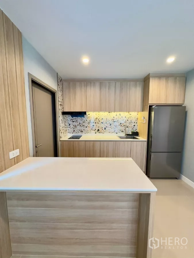 Detached House for rent in Samut Prakan - Contemporary kitchen with island, wood cabinetry, terrazzo backsplash and refrigerator.