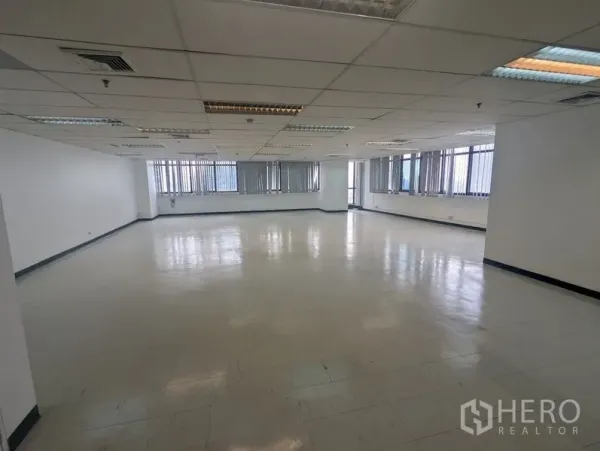 Office Space for rent or sale - Spacious corner office floor with grid ceiling lighting and a wall of windows fitted with vertical blinds.