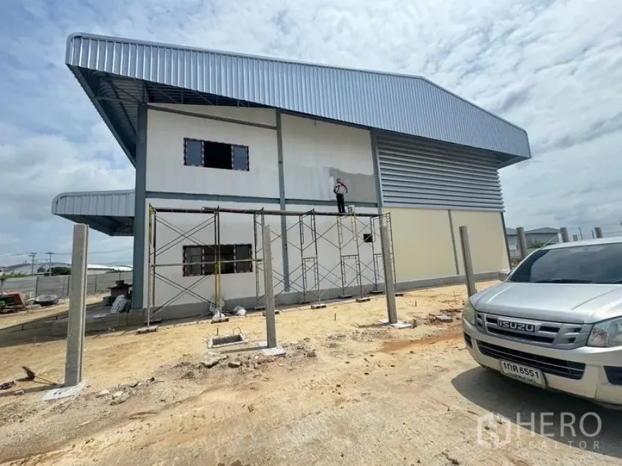 Warehouse for rent in Mueang Samut Prakan, Samut Prakan - Side elevation of the newly built warehouse with metal siding and open yard under cloudy sky.