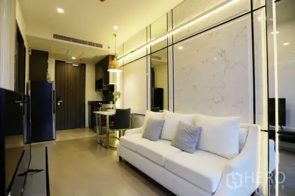 Condominium for rent in Watthana, Bangkok - Open-plan living area with sofa, dining table and compact kitchenette under warm lights.