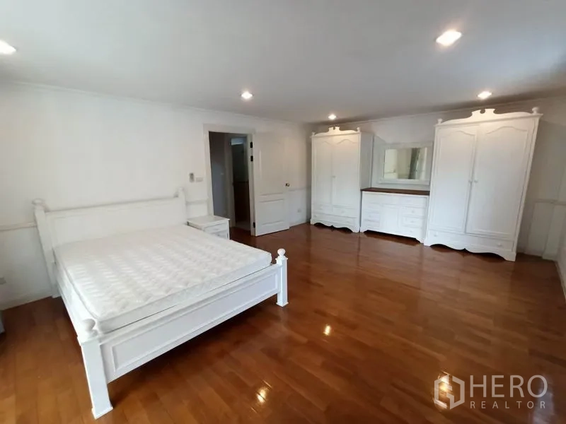 Detached House for rent in Mueang Samut Prakan, Samut Prakan - Spacious master bedroom with wood floors, white bed and full wardrobes.