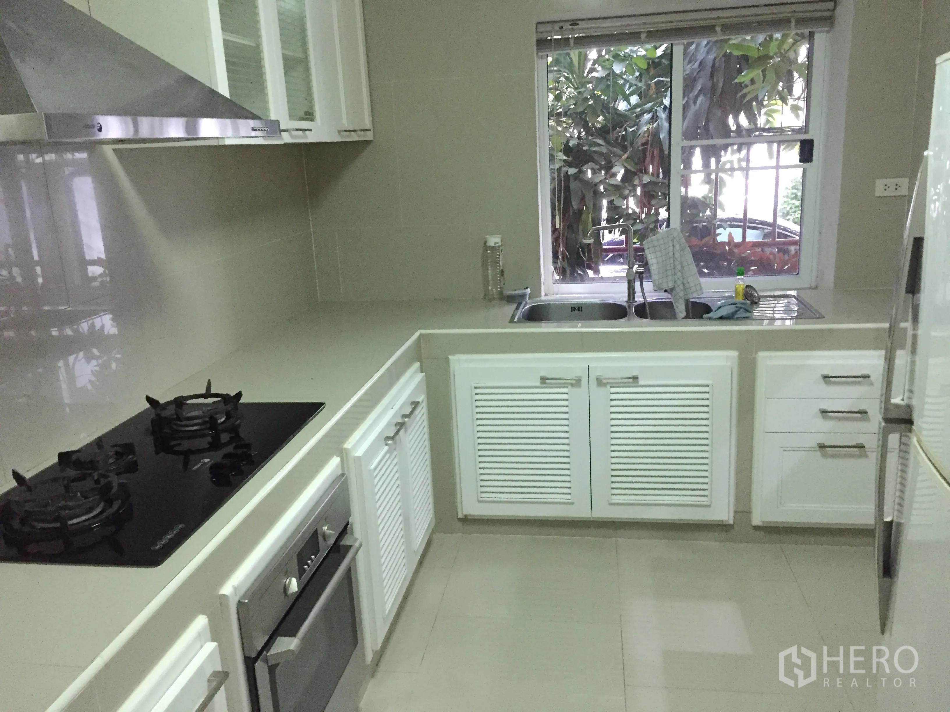 Detached House for rent in Watthana, Bangkok - U-shaped built-in kitchen with gas hob, oven, stainless hood, double sink and window view.