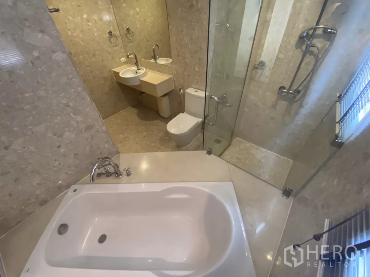 Condominium for rent in Watthana, Bangkok - Marble bathroom showing a bathtub, glass shower enclosure and large wall mirror.