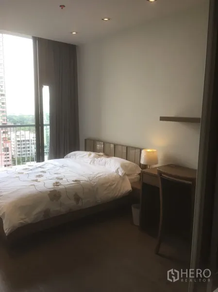 Condominium for rent or sale in Khlong Toei, Bangkok - Bedroom with large window, private balcony and bedside lamp in a modern condo.