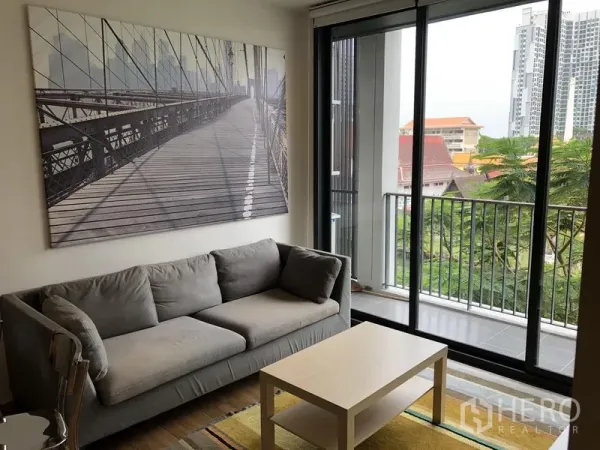 Condominium for rent in Watthana, Bangkok - Sofa corner beside large sliding doors leading to a balcony overlooking greenery.