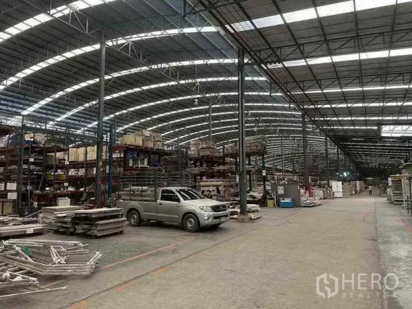 Factory for rent in Pathum Thani - Spacious production hall with arched steel roof, shelving racks and a pickup truck.