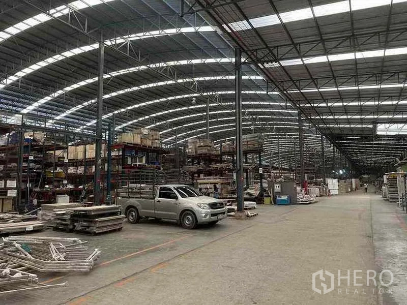 Factory for rent in Pathum Thani - Spacious production hall with arched steel roof, shelving racks and a pickup truck.