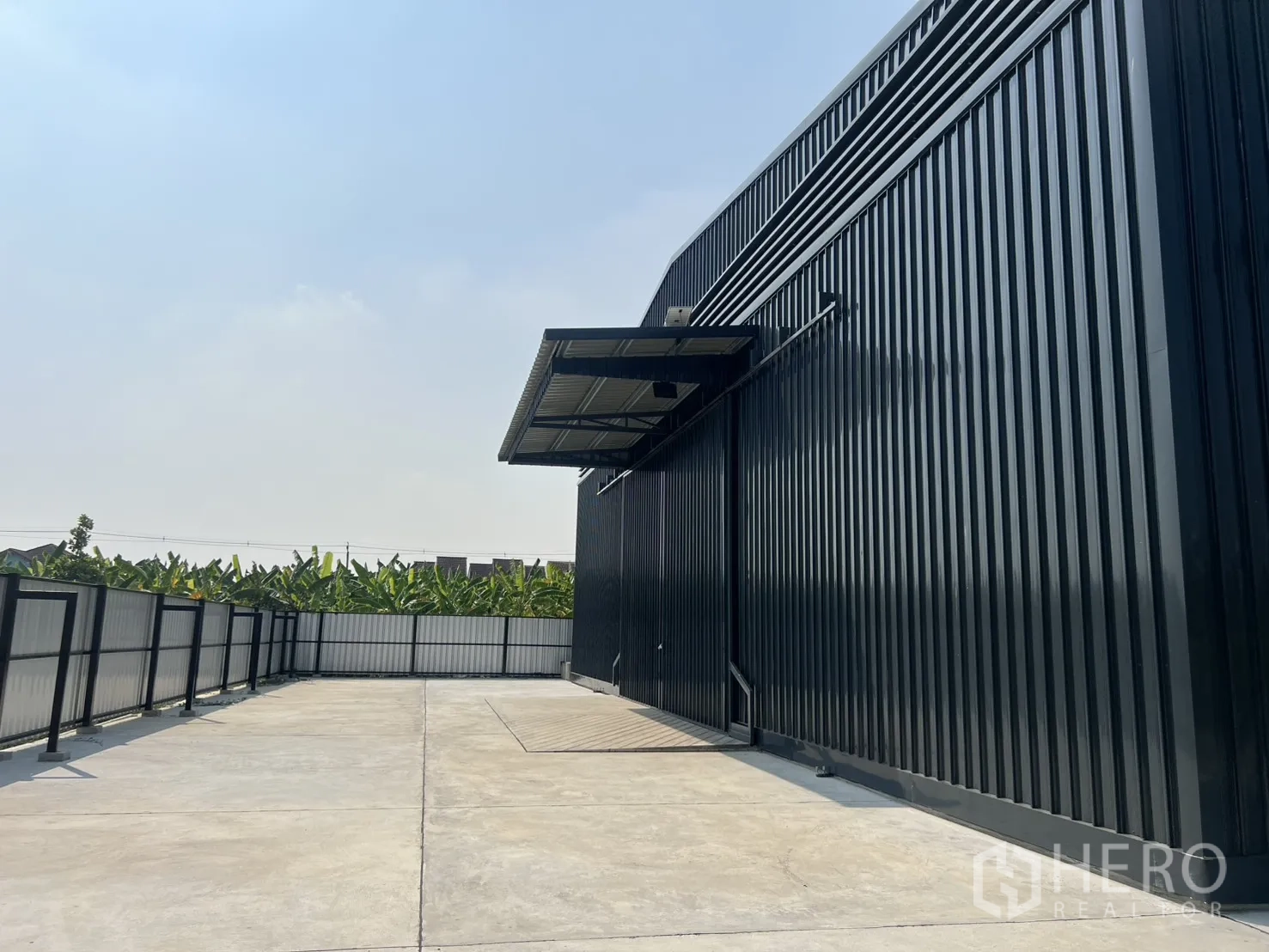 Warehouse for rent in Lat Krabang, Bangkok - Fenced concrete yard beside a black steel warehouse, ample truck turning space and canopy.