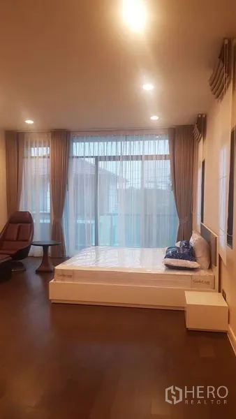 Detached House for rent in Saphan Sung, Bangkok - Spacious master bedroom with floor-to-ceiling windows, bed and lounge chair.