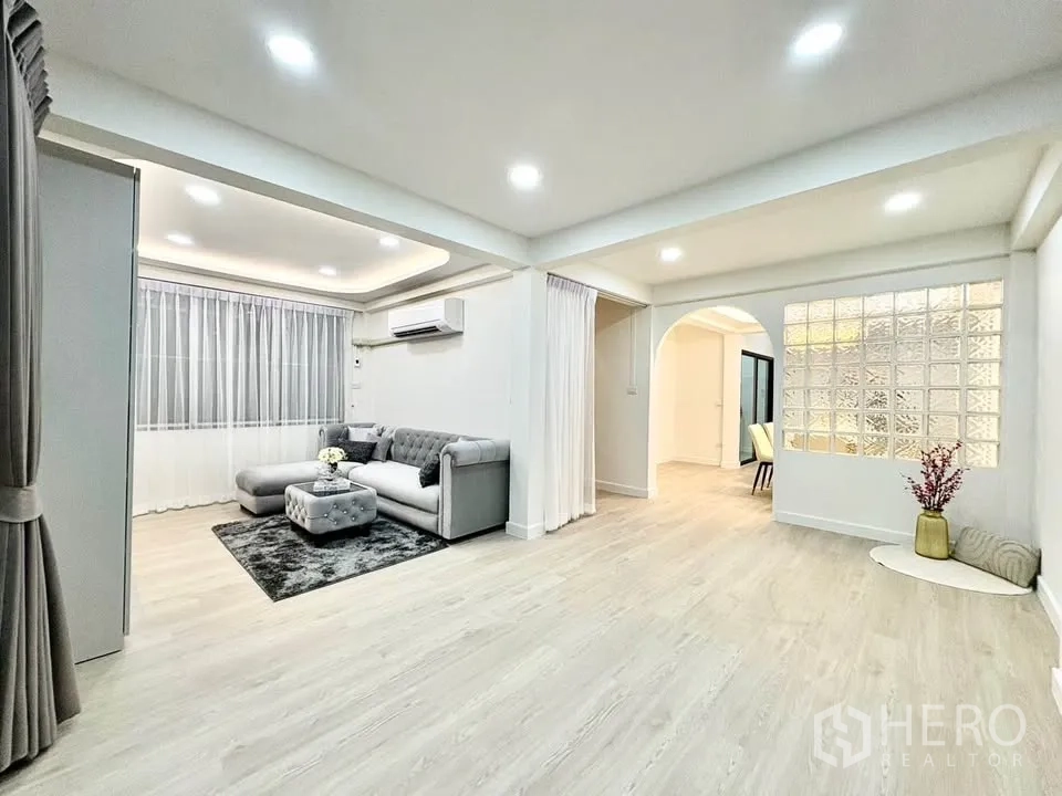 Detached House for rent in Huai Khwang, Bangkok - Open-plan living area with sofa zone, large windows and glass-block feature wall.