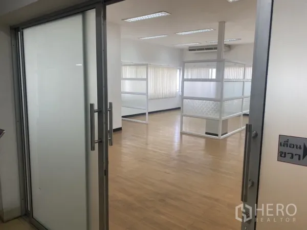 Office Space for rent in Khlong Toei, Bangkok - Entrance view through frosted sliding glass doors into a well-lit office with glass partitions and wood floors.