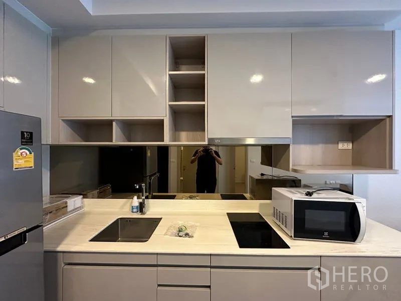 Condominium for rent in Khlong Toei, Bangkok - Modern fitted kitchen with glossy cabinets, induction hob, sink, and microwave in a Khlong Toei condo.