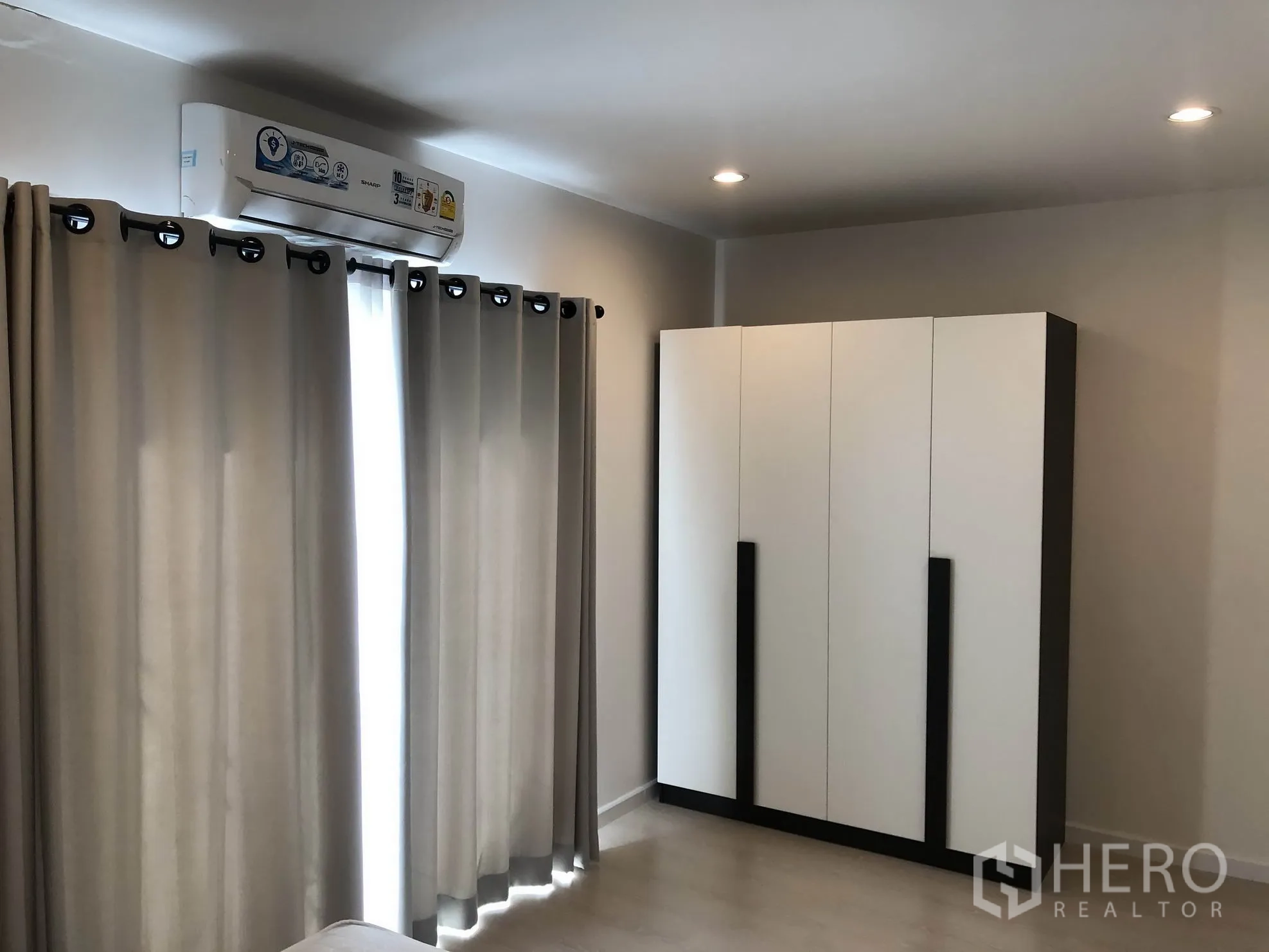 Townhouse for rent in Bang Kapi, Bangkok - Bedroom corner with large wardrobe, curtains and wall-mounted air conditioner under recessed lights.