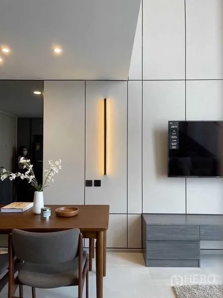 Condominium for rent in Pathum Wan, Bangkok - Minimal dining corner beside a vertical wall sconce and a TV mounted on a paneled feature wall.