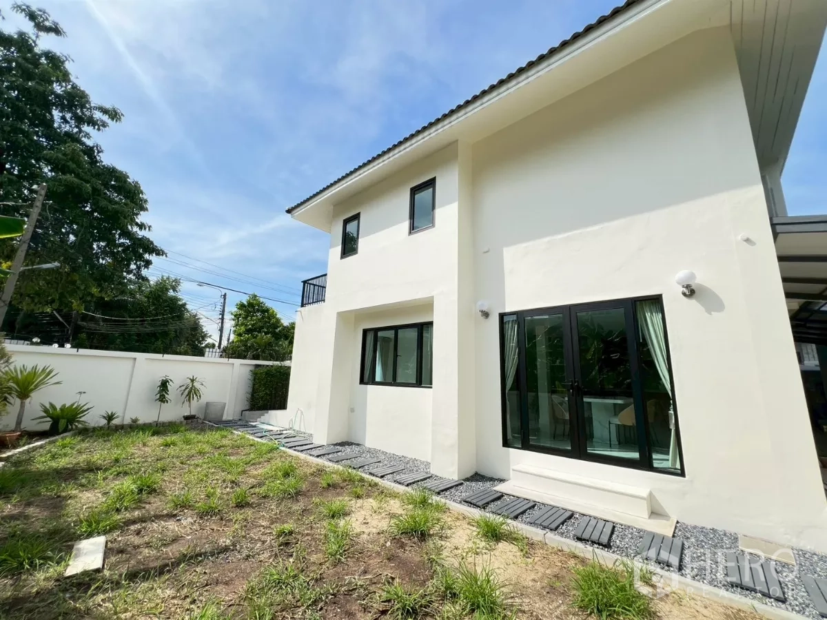 Detached House for rent in Suan Luang, Bangkok - Backyard lawn and pathway beside white boundary wall and sliding doors.
