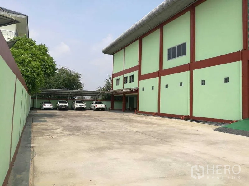 工厂 出租在Mueang Samut Sakhon, Samut Sakhon - 大面积停车院，设有车棚，旁为高仓库外墙。