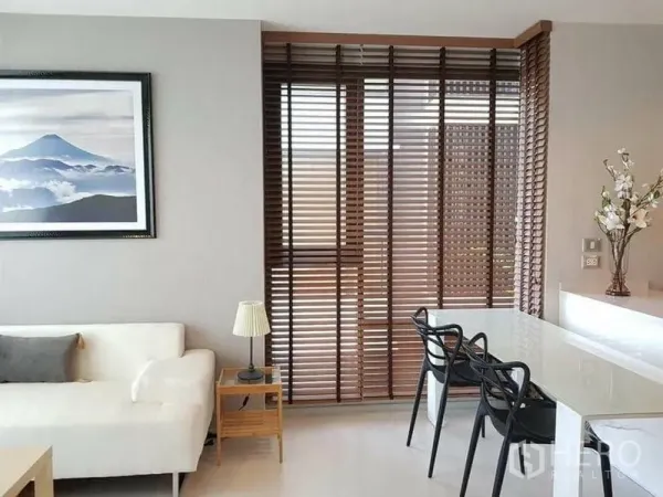 Condominium for rent or sale in Khlong Toei, Bangkok - Dining nook beside floor-to-ceiling wooden blinds and white sofa with wall art.