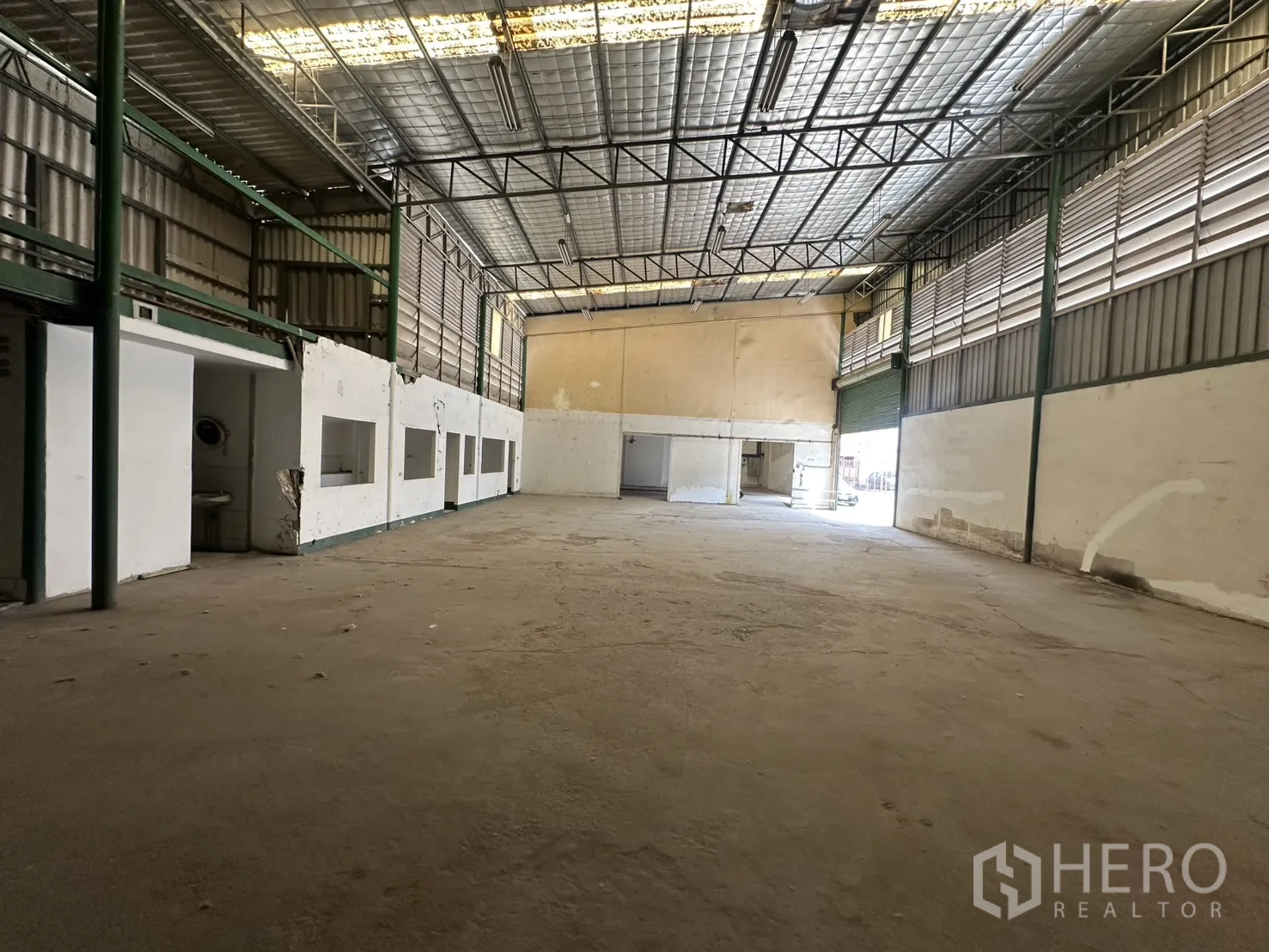 Warehouse for rent in Suan Luang, Bangkok - Open storage hall with partitioned office rooms beneath a mezzanine and insulated roof panels.