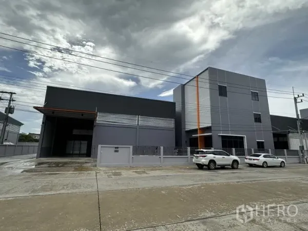 工厂 出租或出售在Lam Luk Ka, Pathum Thani - 现代灰色仓库与办公楼正立面，设停车位与围栏。