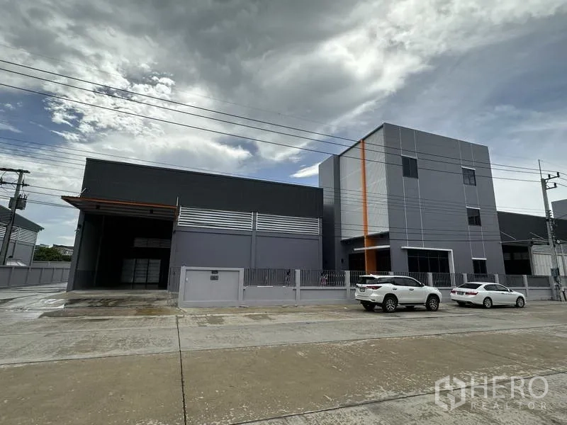 工厂 出租或出售在Lam Luk Ka, Pathum Thani - 现代灰色仓库与办公楼正立面，设停车位与围栏。