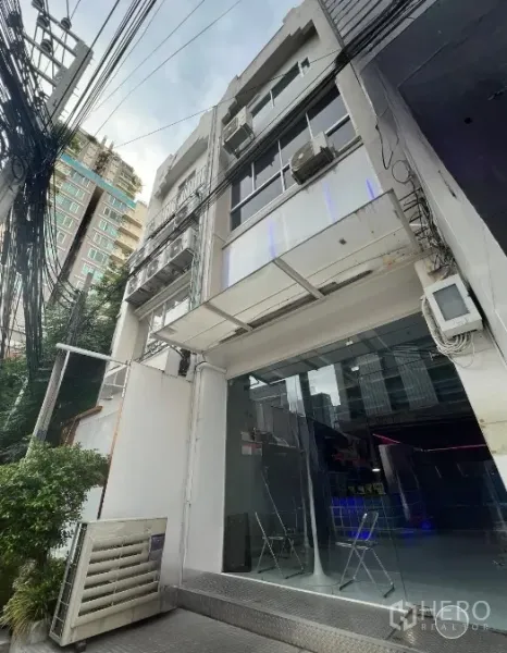 Shophouse for rent or sale in Watthana, Bangkok - Angled exterior of multi-storey shophouse with glass façade and neighboring buildings in Watthana.