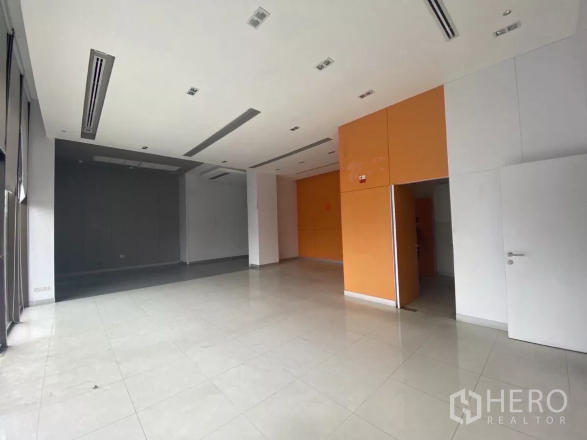 Retail Space for rent in Bang Rak, Bangkok - Spacious retail unit with white ceiling, recessed lighting and an orange accent wall with doorway to back-of-house.
