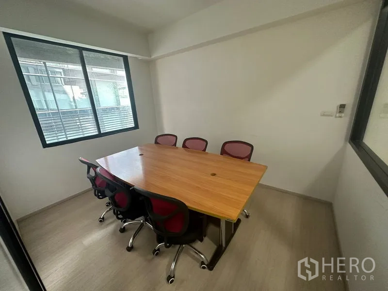 Office Space for rent in Khlong Toei, Bangkok - Compact meeting room with a wooden conference table and six red office chairs beside a window.