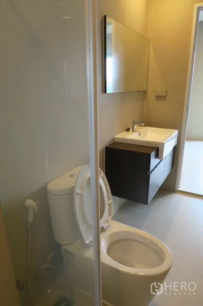 Townhouse for rent in Suan Luang, Bangkok - Modern bathroom with wall-mounted vanity, mirror cabinet, and toilet beside a glass shower.
