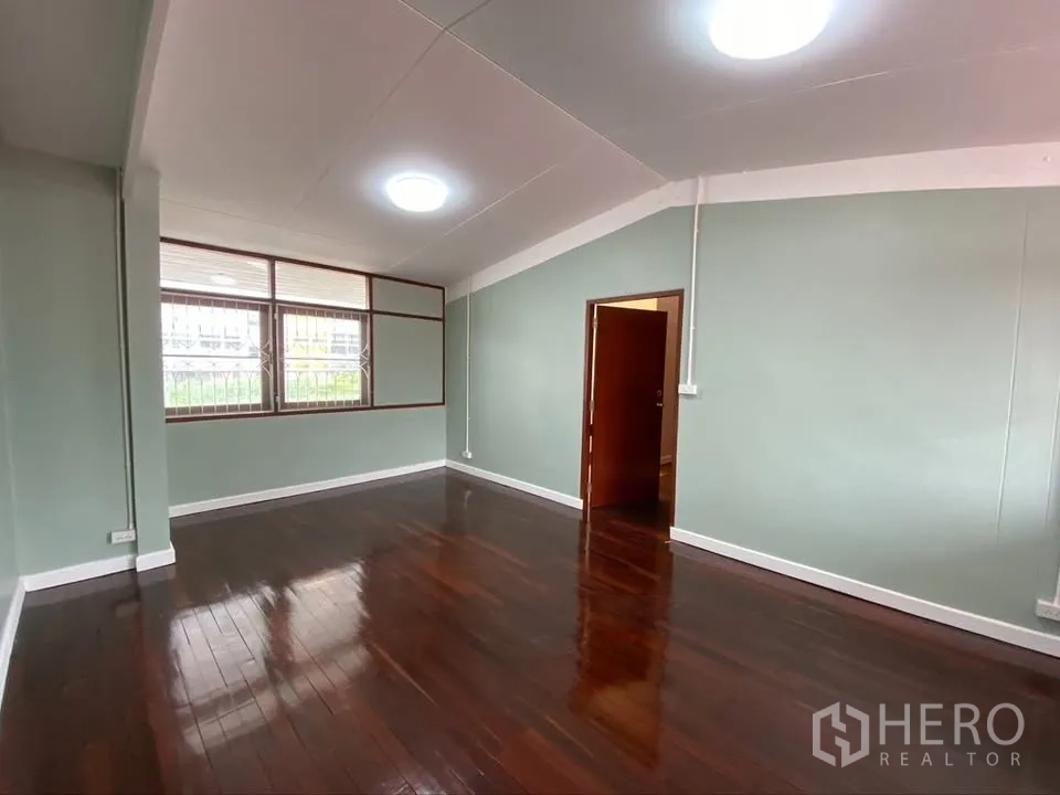独栋房屋 for rent in Suan Luang, Bangkok - 宽敞房间配深色木地板、绿色墙面与大窗户。