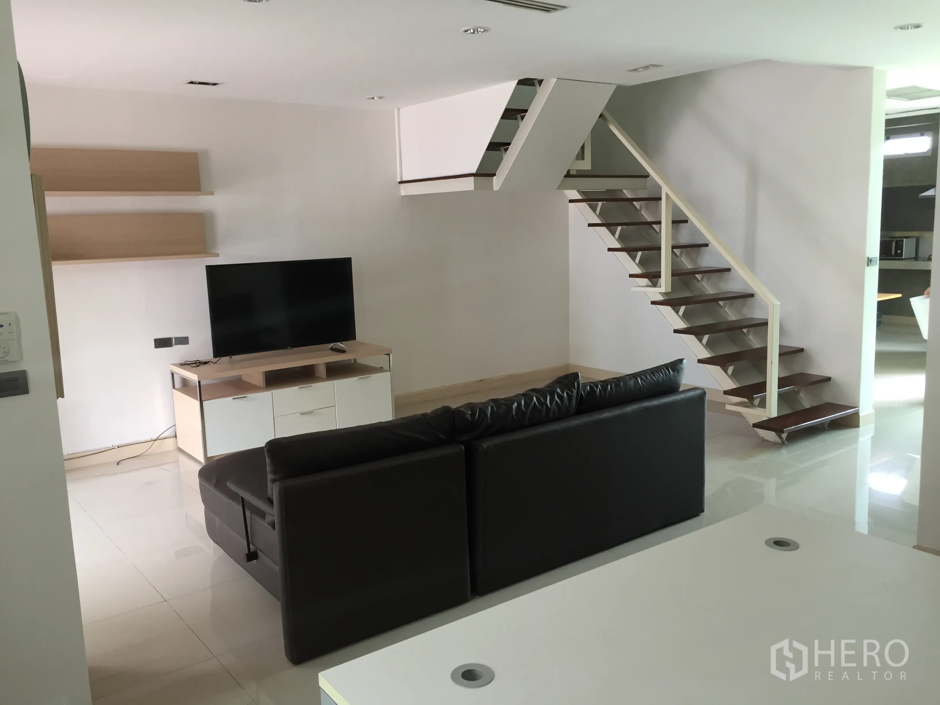 Townhouse for rent in Din Daeng, Bangkok - Living area from another angle showing TV, wall shelves and staircase to the upper floor.