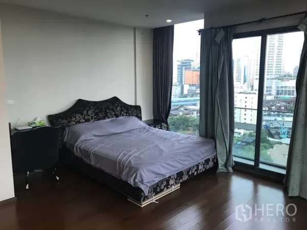 Condominium for rent in Khlong Toei, Bangkok - Master bedroom with large windows, city skyline view and a small desk.