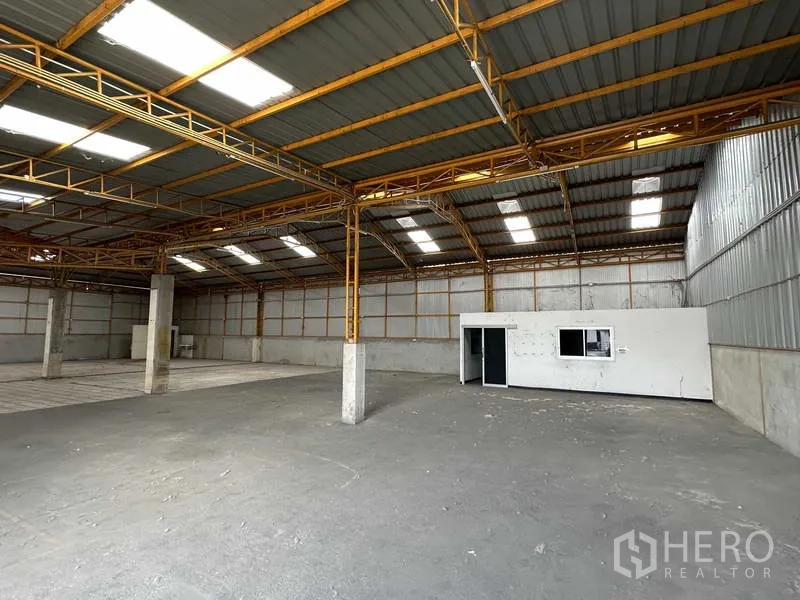 Warehouse for rent in Mueang Pathum Thani, Pathum Thani - Warehouse interior showing a small office room, high ceiling, and ample storage area.