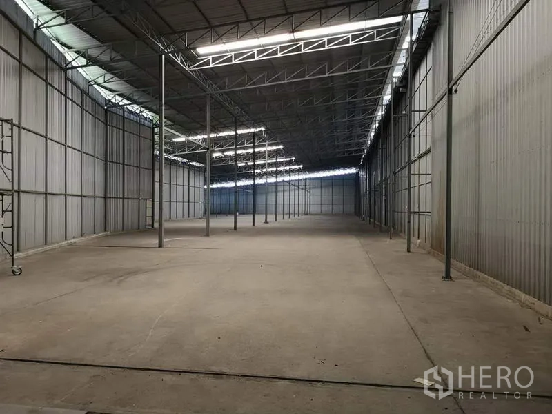 Warehouse for rent in Pak Kret, Nonthaburi - Spacious warehouse interior with a high steel truss roof, skylights, and open concrete floor.