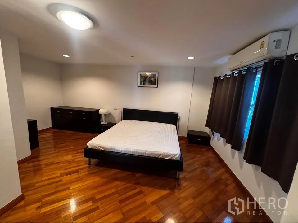 Townhouse for rent in Huai Khwang, Bangkok - Bedroom with bed, wood floors, dark curtains and air conditioning.