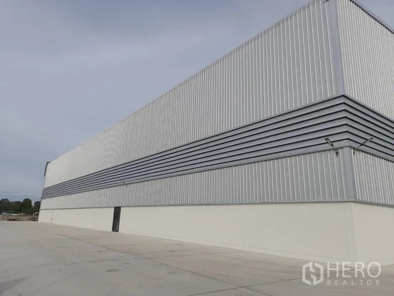 Factory for rent in Mueang Rayong, Rayong - Long exterior wall of steel-clad building with expansive concrete apron for truck circulation.