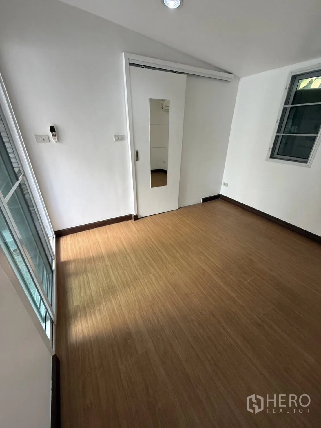 Detached House for rent in Khlong Toei, Bangkok - Bedroom with wood-style flooring, a sliding door with mirror, and a window.