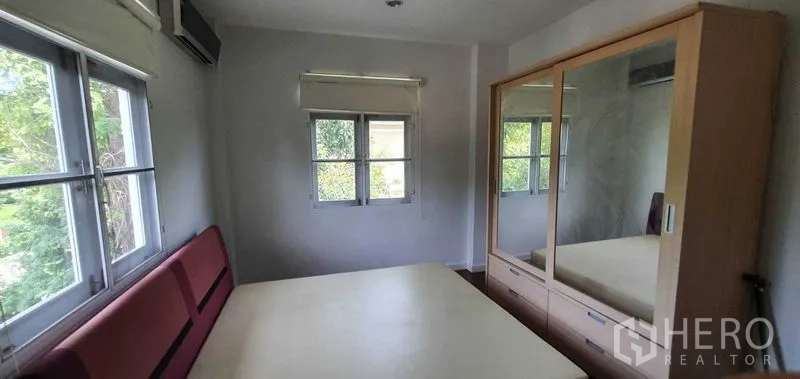 Detached House for rent in Prawet, Bangkok - Compact bedroom with mirrored wardrobe and garden views through twin windows.