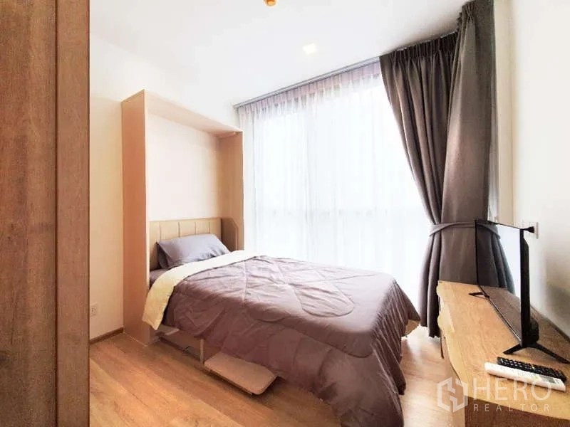 Condominium for sale in Watthana, Bangkok - Second bedroom with bed, blackout curtains and TV on a wooden cabinet.