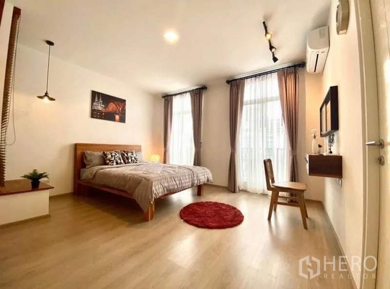 Townhouse for rent in Bang Phli, Samut Prakan - Spacious master bedroom with wood bed, large windows, sheer curtains and balcony doors.