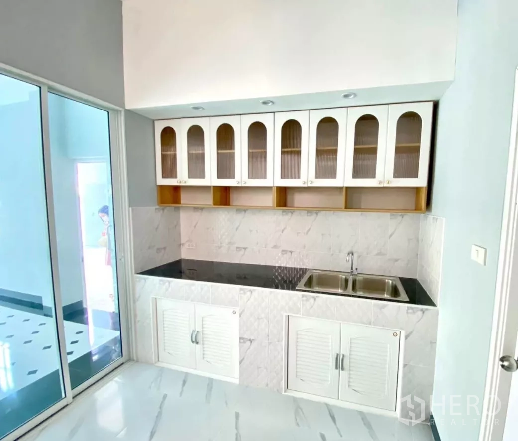 Factory for rent or sale in Bang Bua Thong, Nonthaburi - Compact kitchen with upper cabinets, black countertop and double sink.