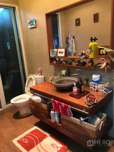 Detached House for sale in Lat Phrao, Bangkok - Bathroom with vessel sink on wooden vanity, large mirror and toilet next to a glass door.