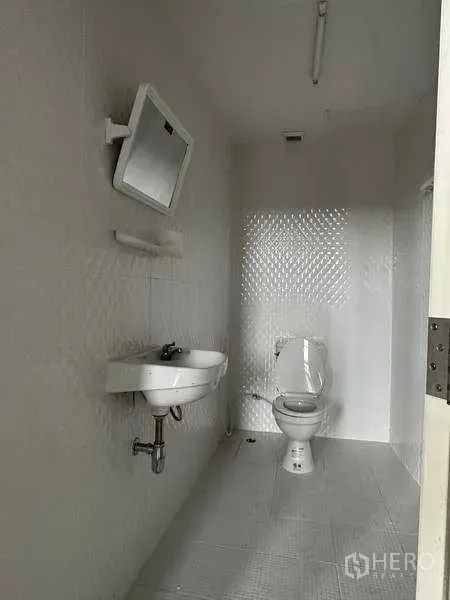 Warehouse for rent in Samut Prakan - Simple restroom with toilet, sink, wall mirror and white tiled finishes.