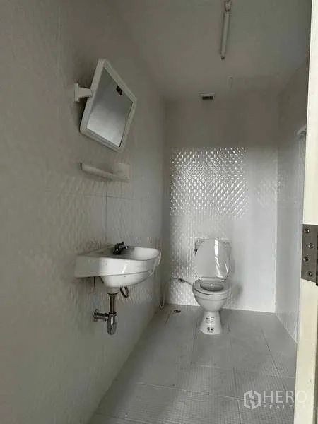 Warehouse for rent in Samut Prakan - Simple restroom with toilet, sink, wall mirror and white tiled finishes.