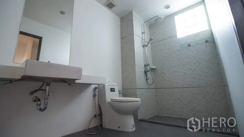 Townhouse for rent or sale in Phra Khanong, Bangkok - Bright bathroom with wall-mounted sink, toilet and a walk-in shower with a glass-block window.
