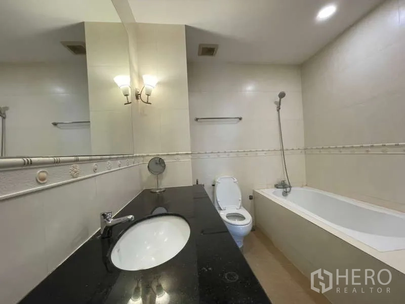 Apartment for rent in Khlong Toei, Bangkok - Bathroom with long vanity, bathtub with shower, and wall mirror.