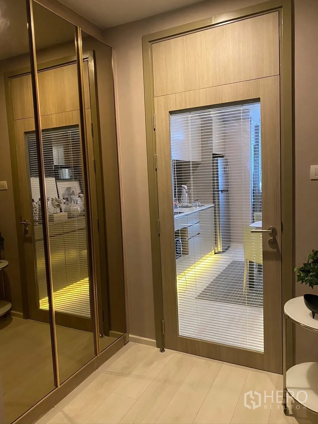 Condominium for rent in Pathum Wan, Bangkok - Entry hallway with mirrored wardrobe and a glass door leading to the kitchen with warm lighting.