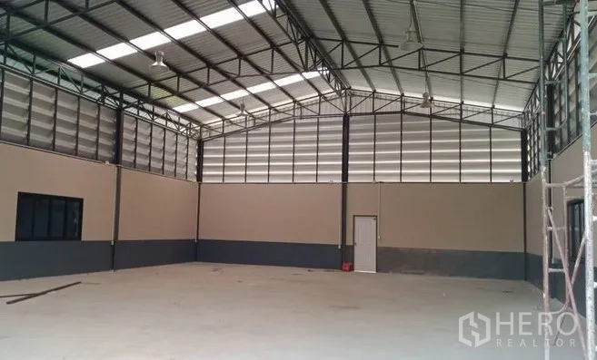คลังสินค้า ขายในPathum Thani - มุมโกดังโล่ง แสดงโครงถักเหล็ก ผนังระบายอากาศแบบบานเกล็ด และประตูด้านข้าง