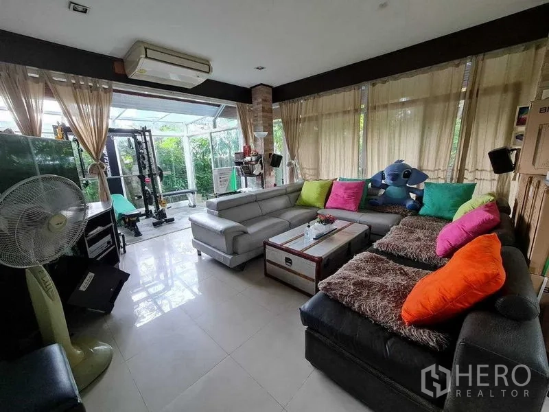 Detached House for sale in Bang Na, Bangkok - Spacious lounge with sectional sofas and large windows opening to greenery.